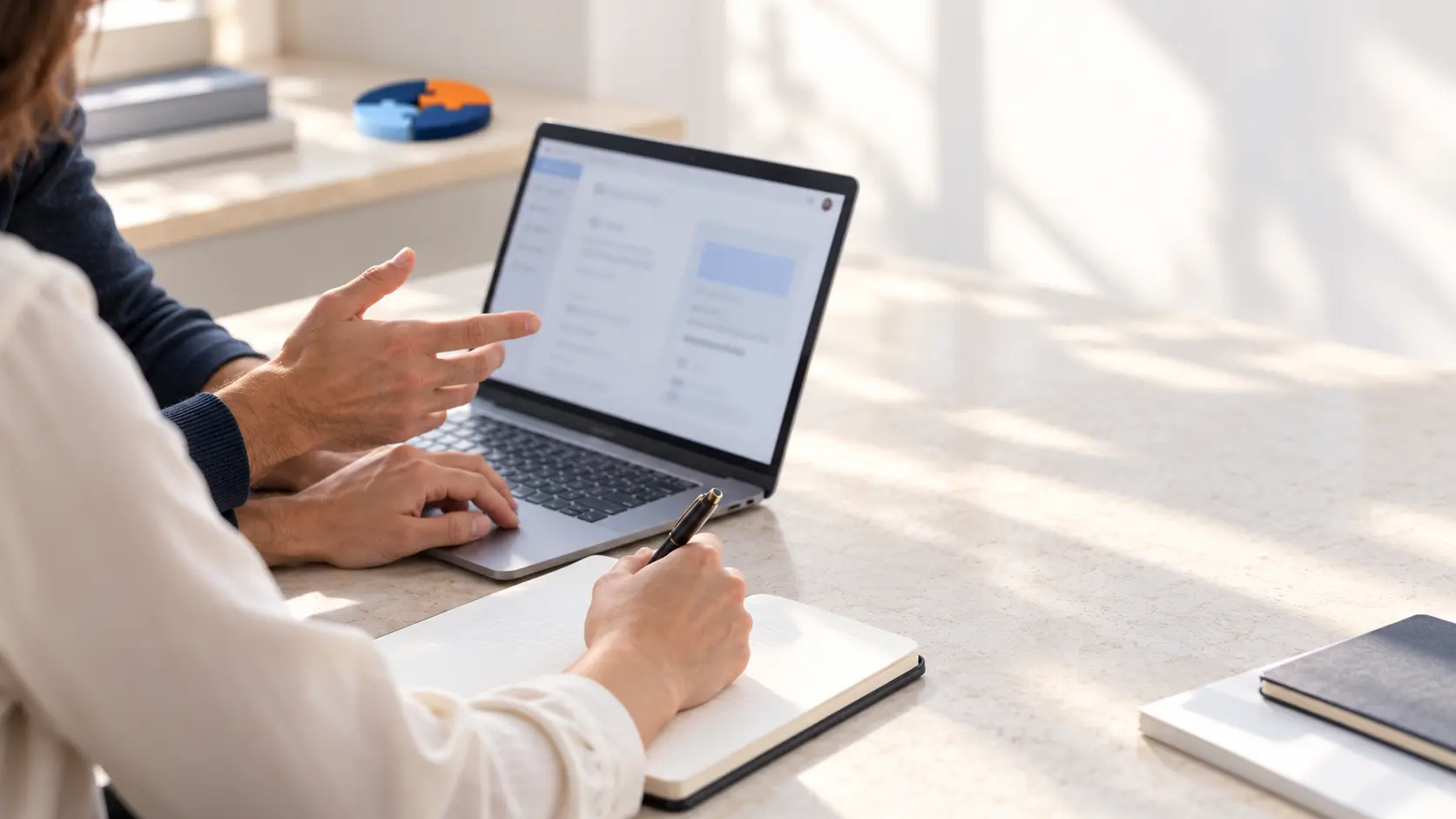 Two colleagues collaborating at a laptop, with a small puzzle detail in the background